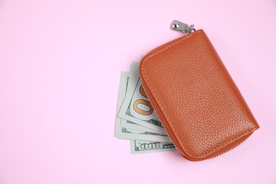Photo of Stylish brown leather purse with dollar banknotes on pink background, flat lay. Space for text