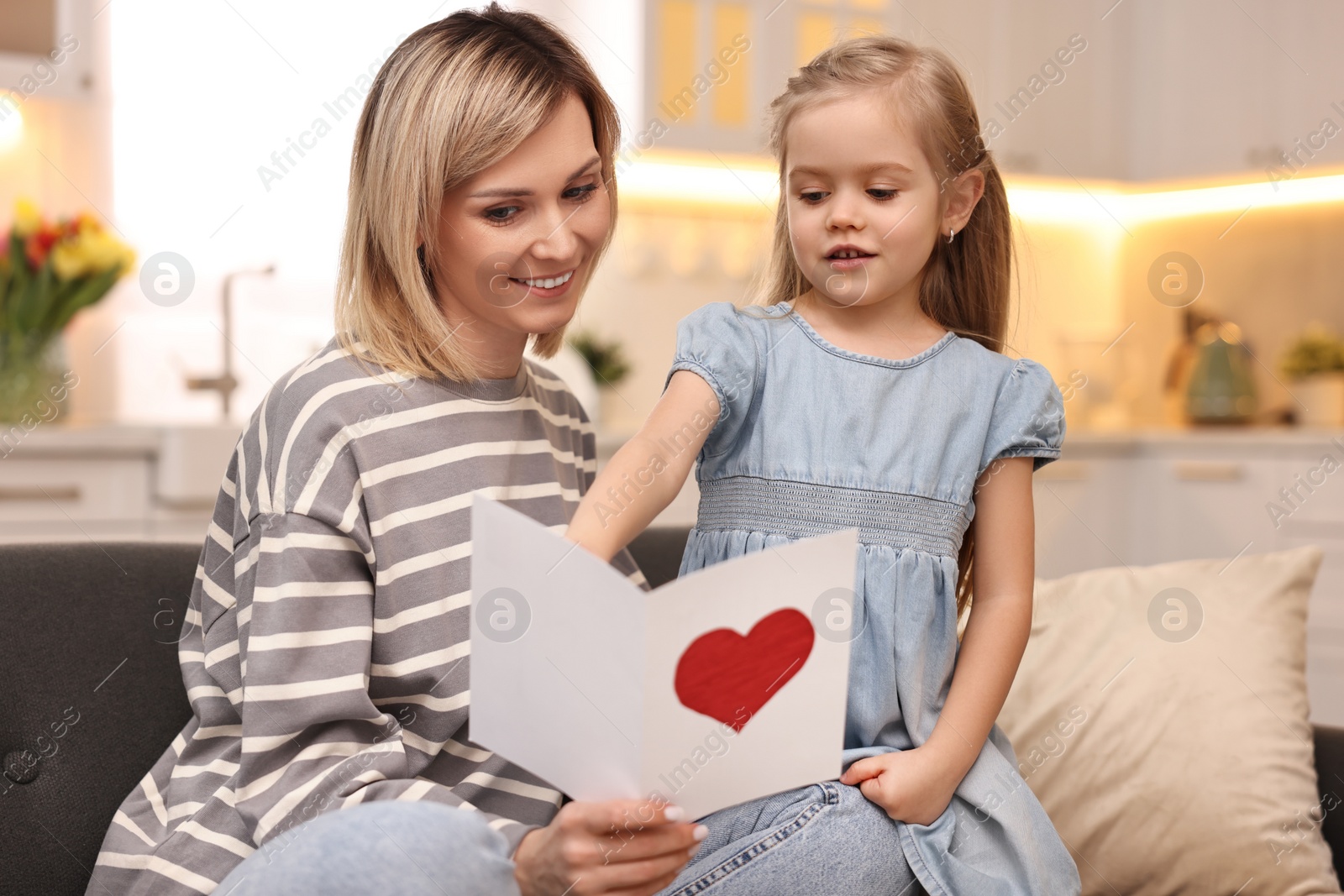 Photo of Little daughter congratulating her mom with greeting card at home. Happy Mother's Day