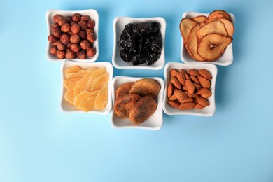 Photo of Bowls with dried fruits and nuts on light blue background, flat lay. Space for text