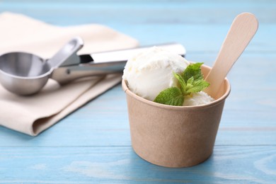 Delicious vanilla ice cream with mint in paper cup on light blue wooden table, closeup. Space for text