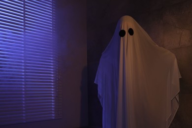 Photo of Creepy ghost. Woman covered with sheet near window in color lights, space for text
