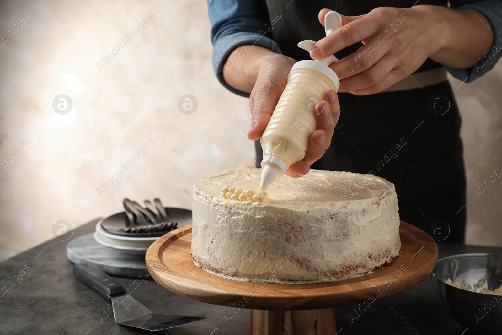 Photo of Woman decorating delicious cake with fresh cream at table indoors, closeup. Homemade pastry