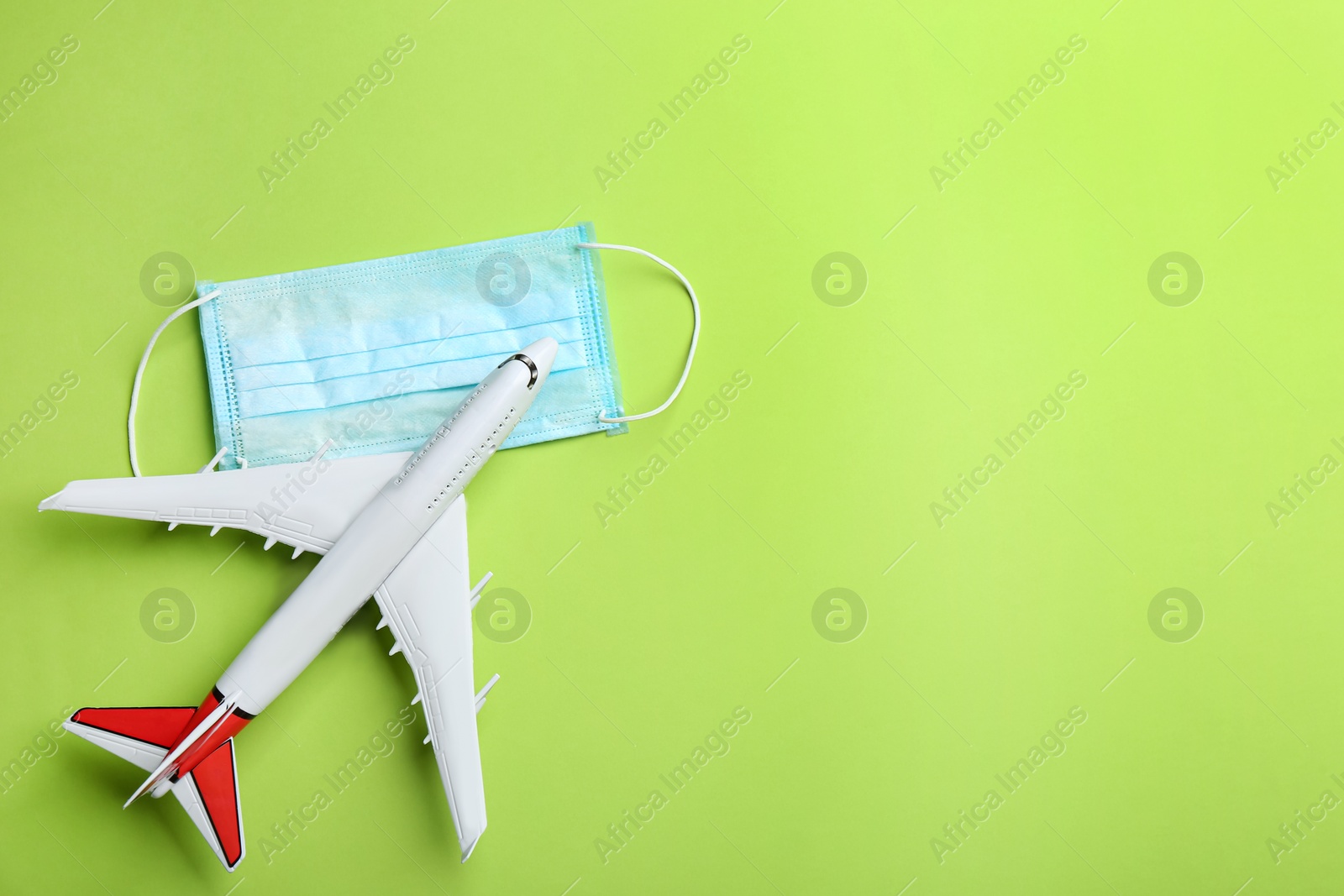 Photo of Toy airplane and protective mask on green background, flat lay with space for text. Travelling during coronavirus pandemic