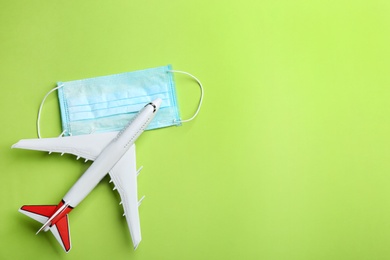 Toy airplane and protective mask on green background, flat lay with space for text. Travelling during coronavirus pandemic