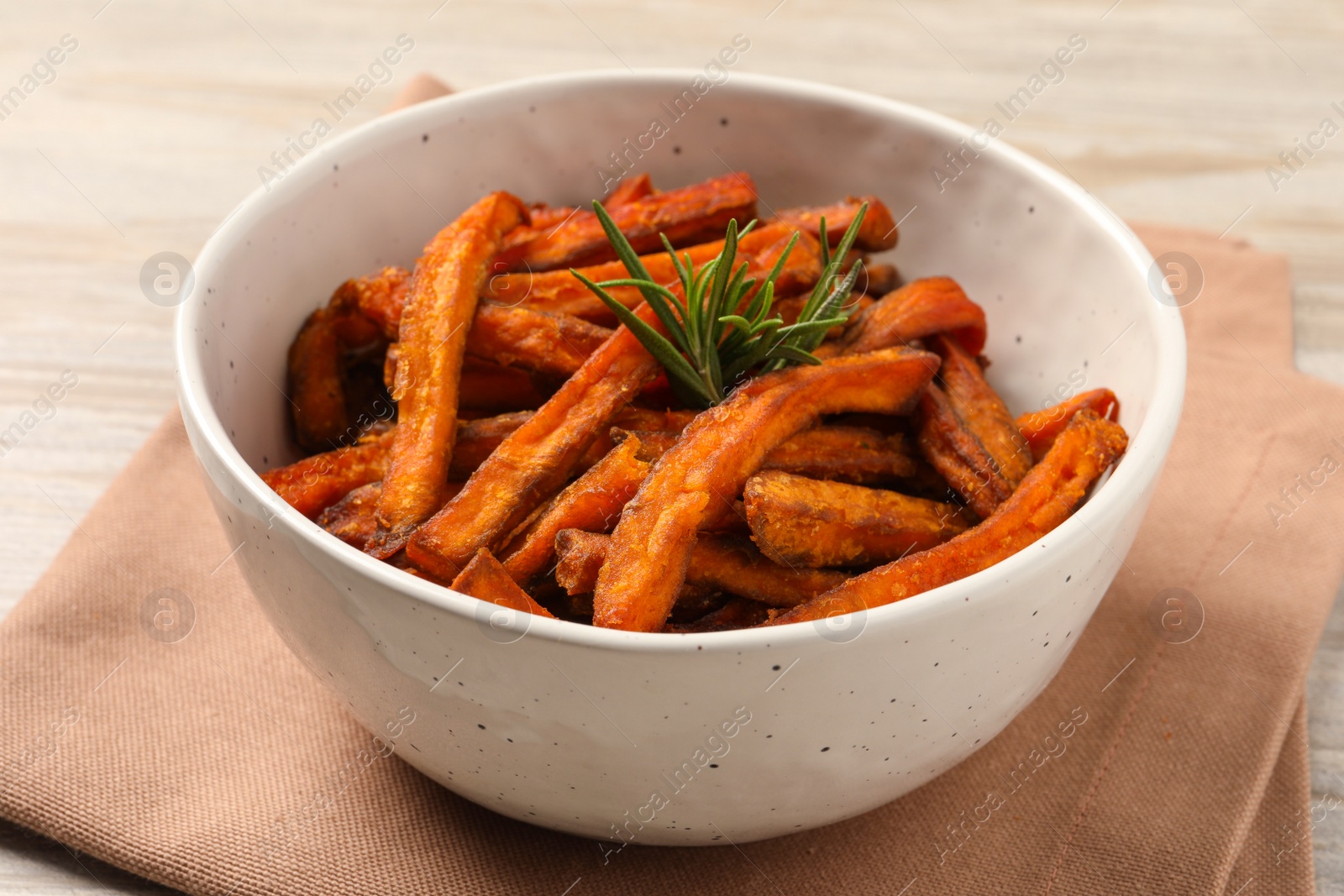 Photo of Bowl with sweet potato fries and rosemary on wooden table, closeup