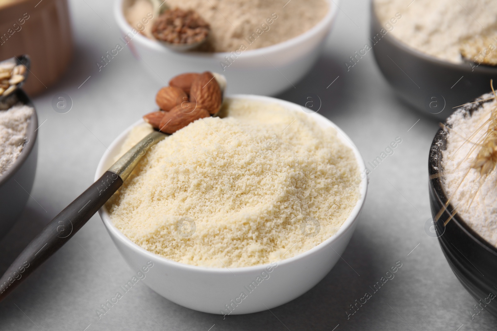 Photo of Bowls with different types of flour and ingredients on light grey table, closeup