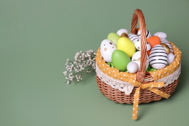 Photo of Wicker basket with festively decorated Easter eggs and gypsophila flowers on pale green background. Space for text