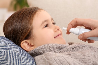 Photo of Mother using nasal spray to treat her little daughter on sofa, closeup