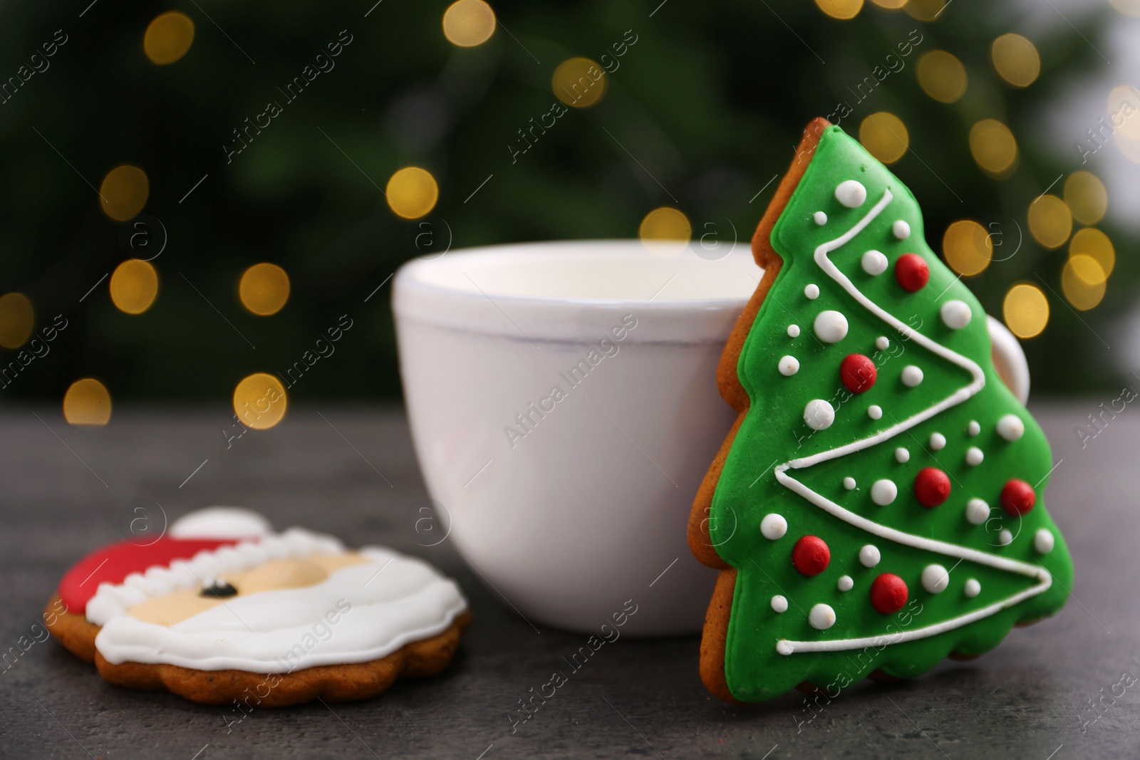 Photo of Decorated cookies and hot drink on grey table against blurred Christmas lights