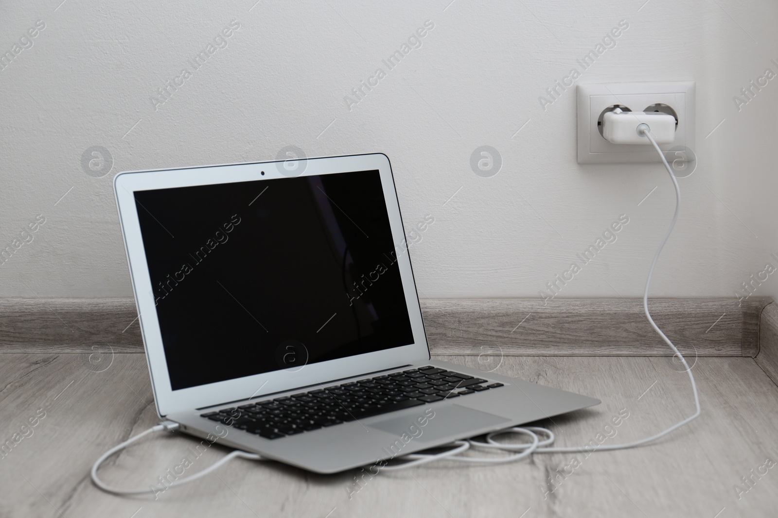 Photo of Modern laptop charging from electric socket on floor