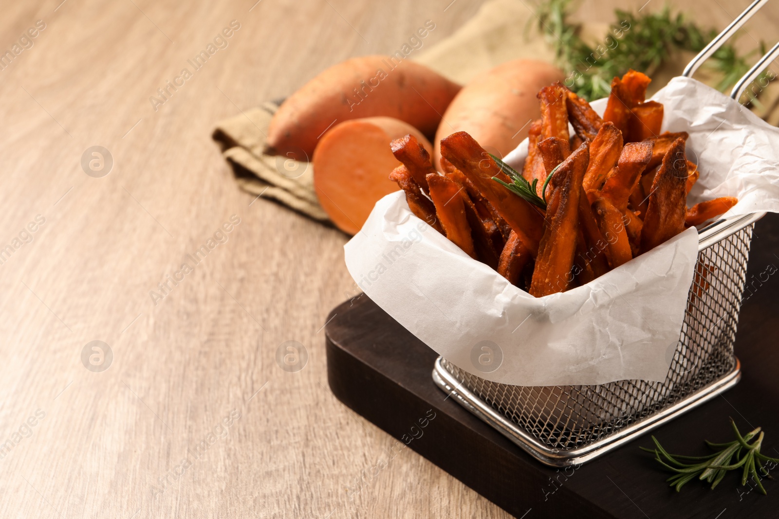 Photo of Frying basket with sweet potato fries on wooden table, closeup. Space for text