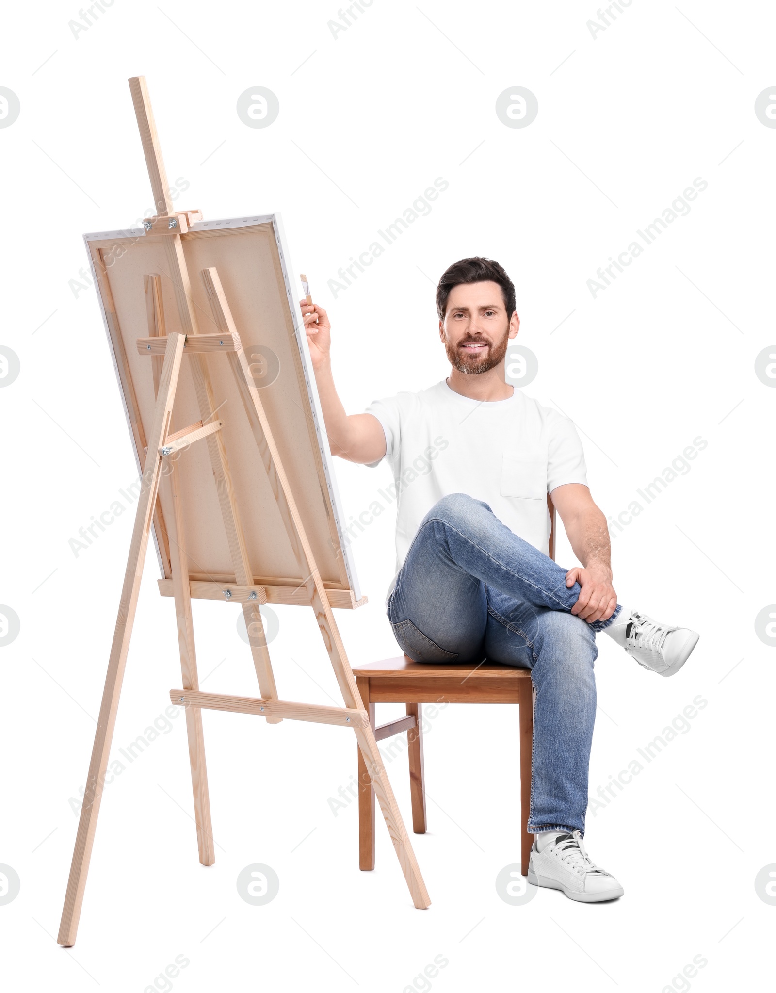 Photo of Happy man painting with brush against white background. Using easel to hold canvas