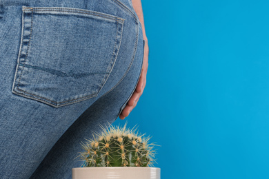 Man sitting down on cactus against light blue background, space for text. Hemorrhoid concept