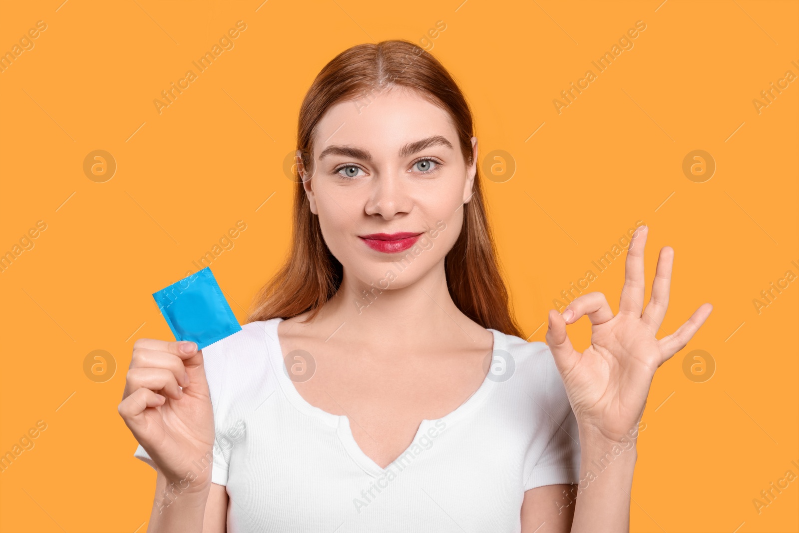Photo of Woman with condom showing ok gesture on yellow background. Safe sex