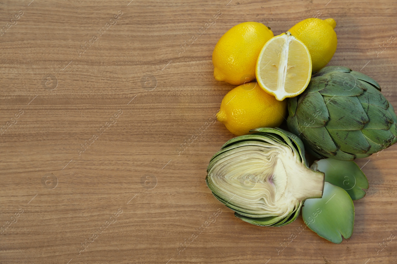 Photo of Artichokes and lemons on wooden table, flat lay. Space for text