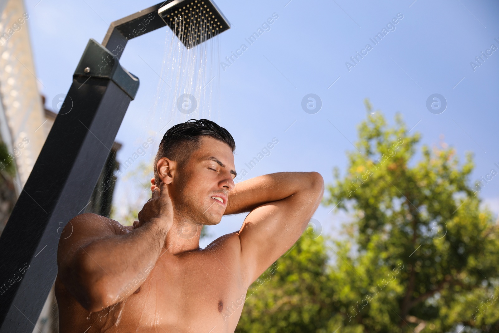 Photo of Man washing hair in outdoor shower on summer day