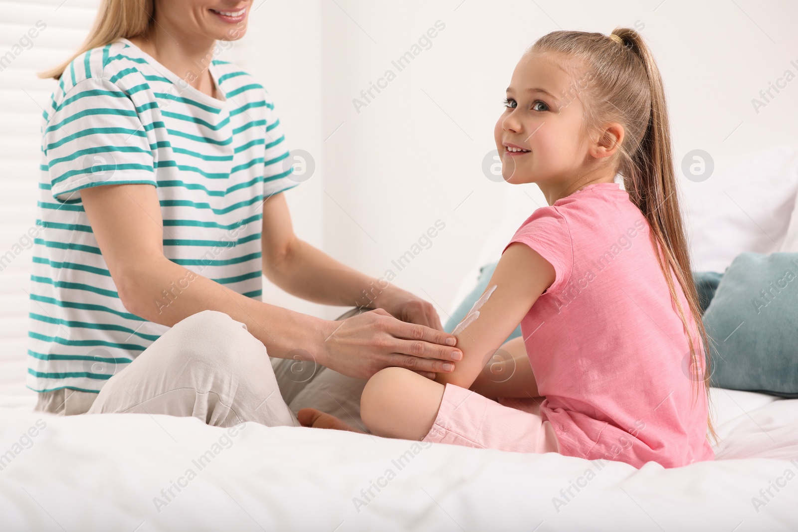 Photo of Mother applying ointment onto her daughter's hand on bed