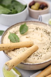 Delicious hummus with grissini sticks on light grey table, closeup