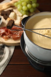 Fondue with tasty melted cheese, forks and piece of bread on wooden table