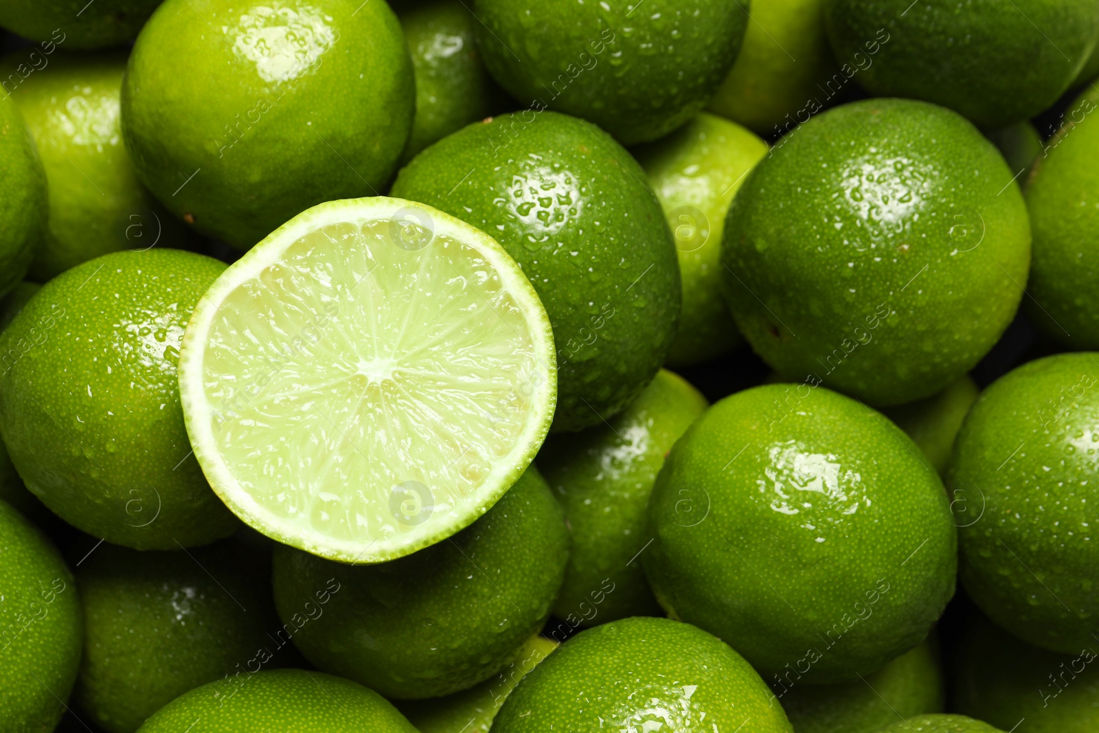 Photo of Whole and cut fresh limes with water drops as background, top view