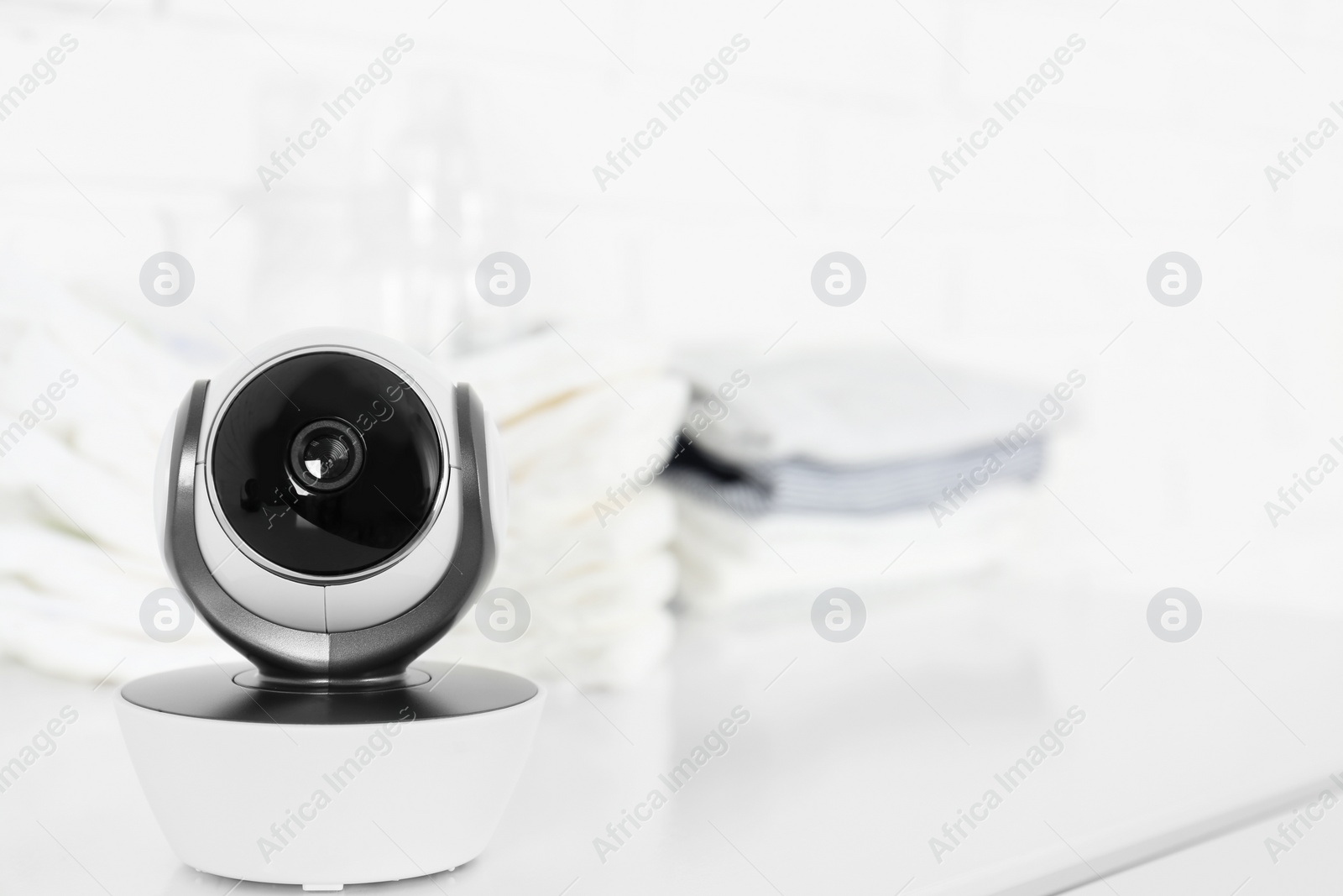 Photo of Baby camera on table near white brick wall, space for text. Video nanny