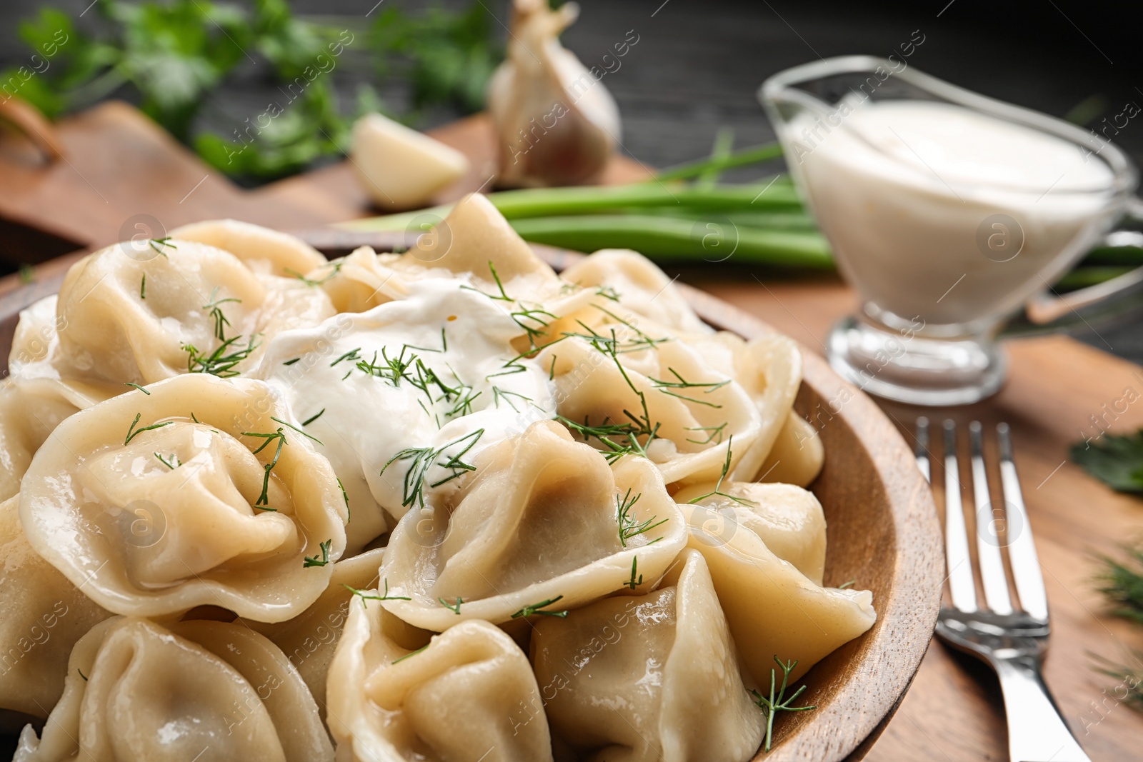 Photo of Tasty dumplings with sour cream in bowl on table, closeup