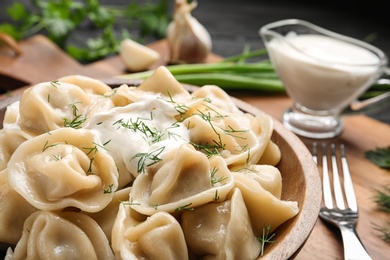 Photo of Tasty dumplings with sour cream in bowl on table, closeup