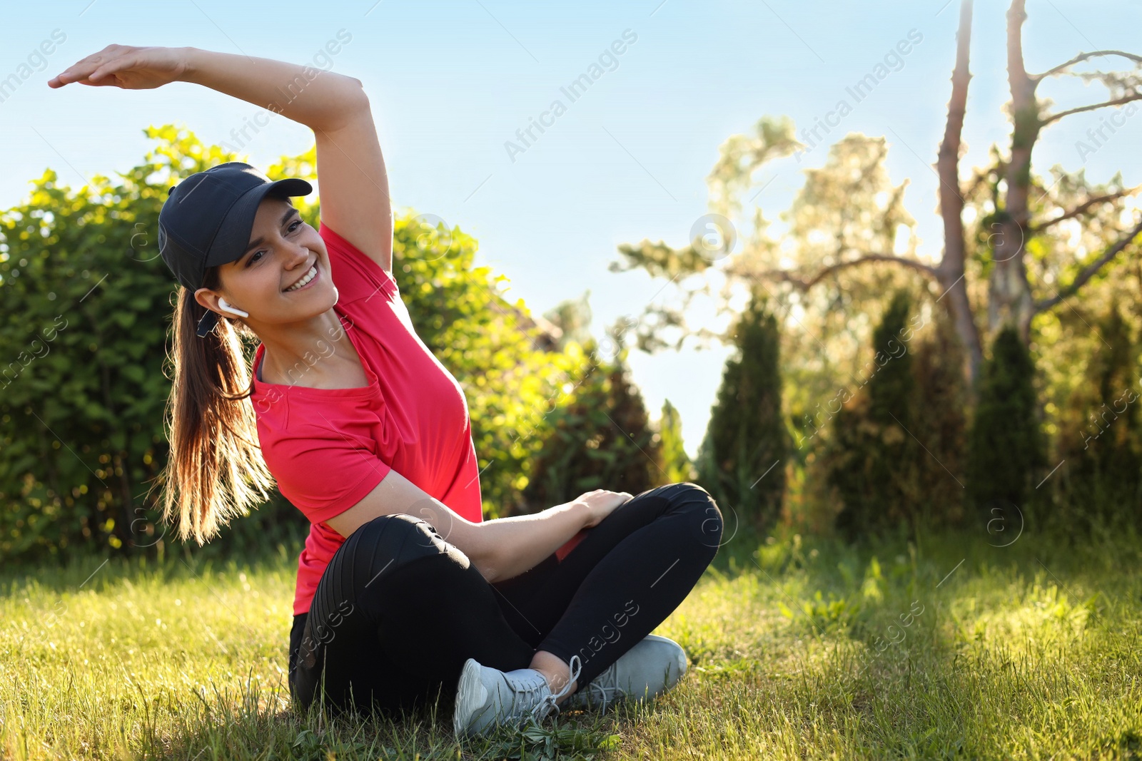 Photo of Young woman listening to music while doing morning exercise on green grass in park, space for text