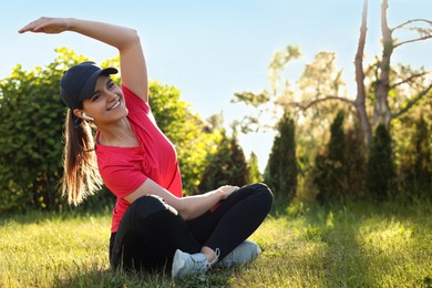 Photo of Young woman listening to music while doing morning exercise on green grass in park, space for text