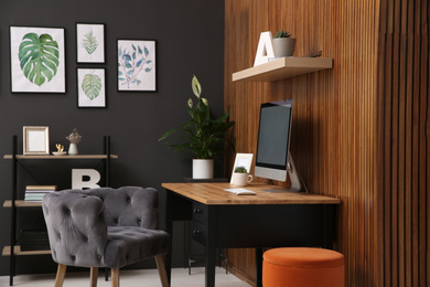 Comfortable workplace with computer near wooden wall in stylish room interior. Home office design