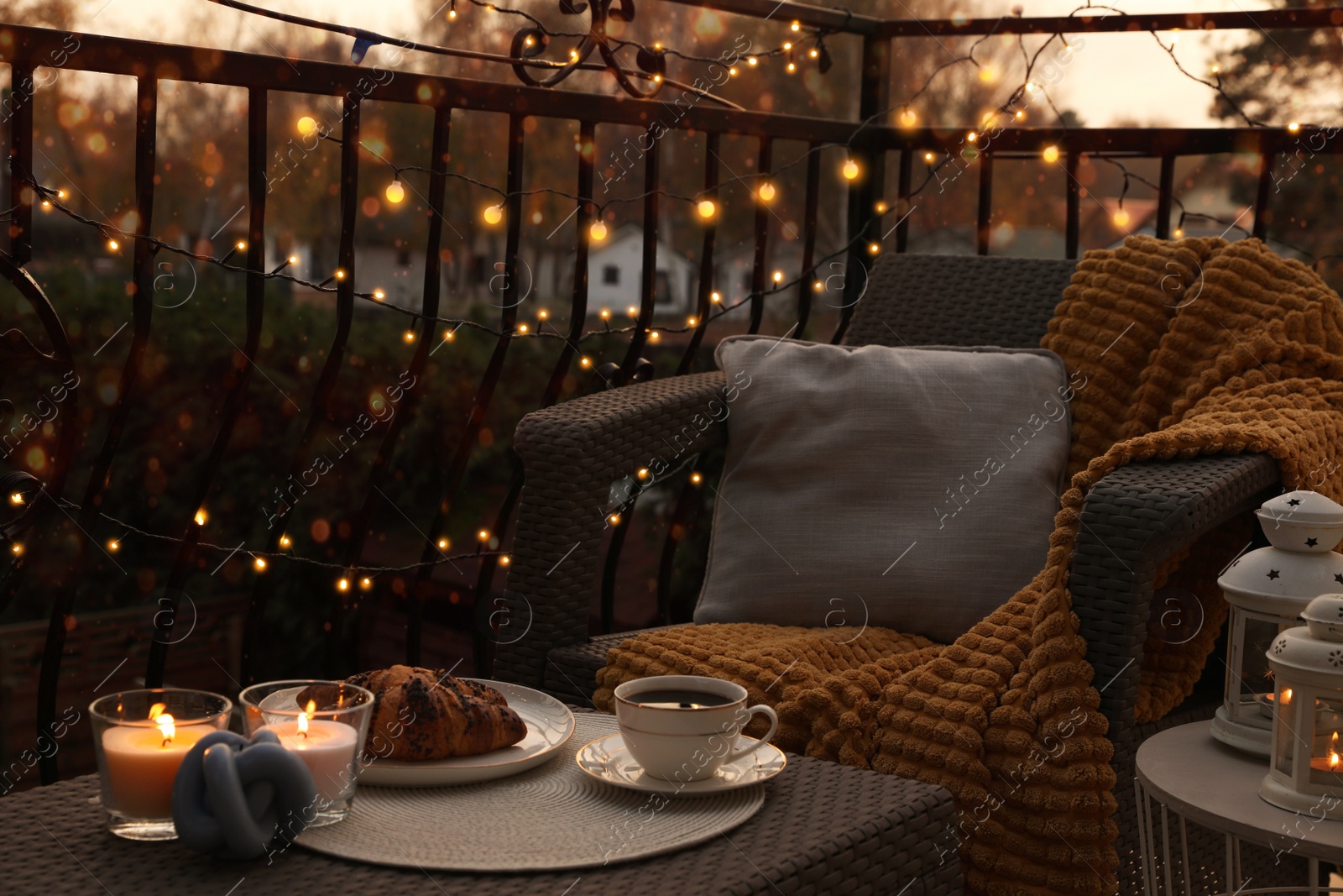 Photo of Beautiful view of garden furniture with pillow, soft blanket and burning candles at balcony