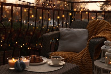 Photo of Beautiful view of garden furniture with pillow, soft blanket and burning candles at balcony