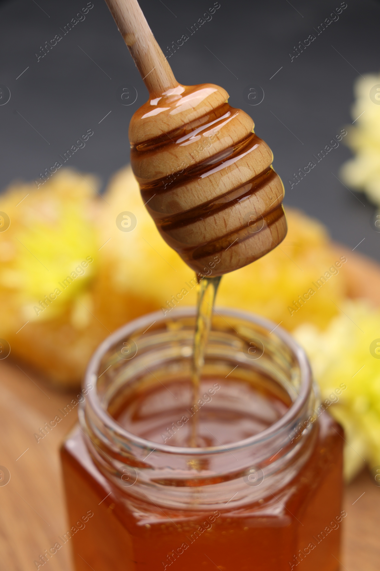 Photo of Pouring sweet honey from dipper into jar at table, closeup