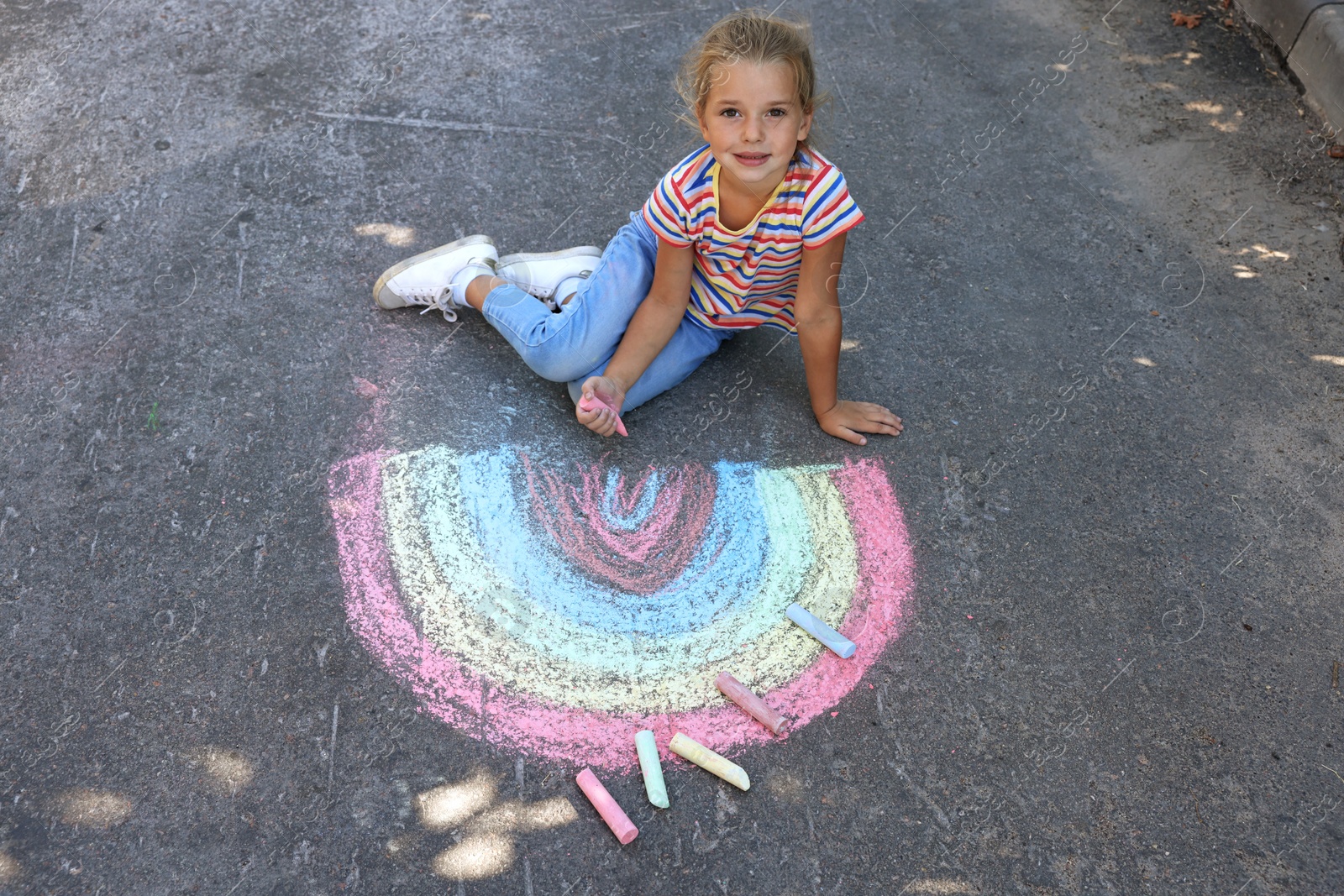 Photo of Cute little child drawing rainbow with colorful chalk on asphalt