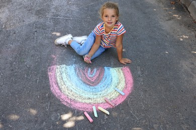 Photo of Cute little child drawing rainbow with colorful chalk on asphalt