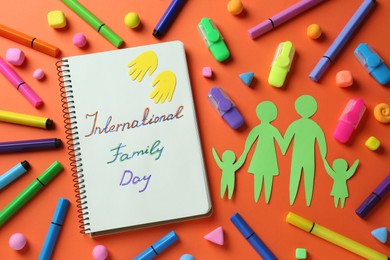 Photo of Happy International Family Day. Flat lay composition with notebook and paper people cutout on orange background