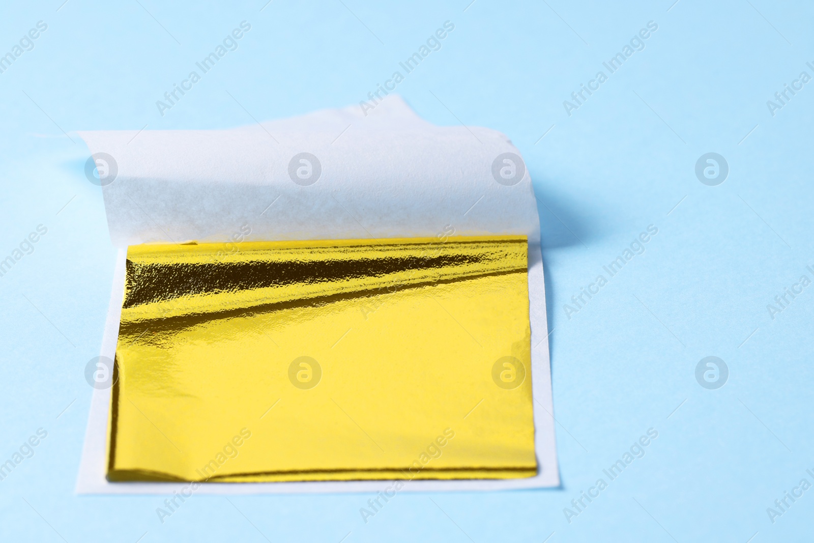 Photo of Edible gold leaf sheet on light blue background, closeup