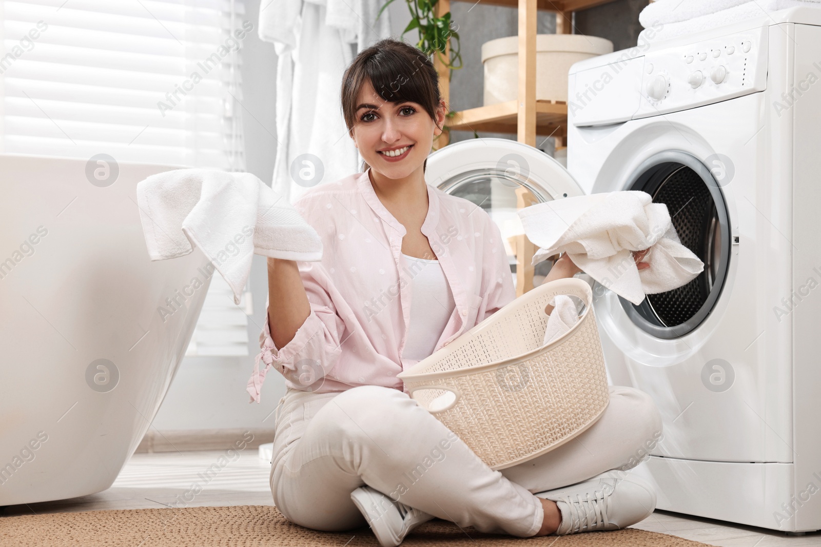 Photo of Happy young housewife with laundry near washing machine at home