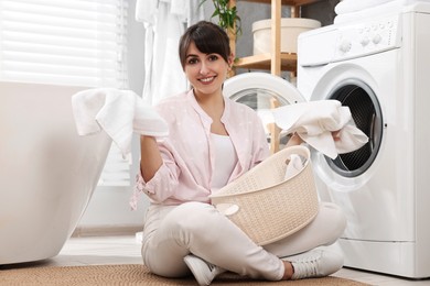 Happy young housewife with laundry near washing machine at home