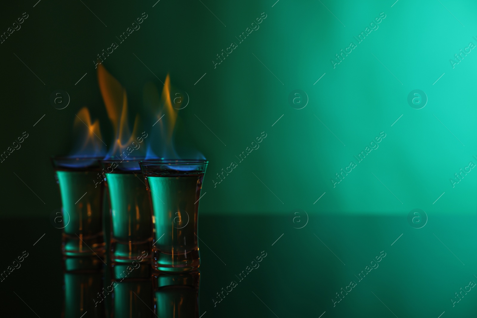 Photo of Flaming vodka in shot glasses on green background, space for text