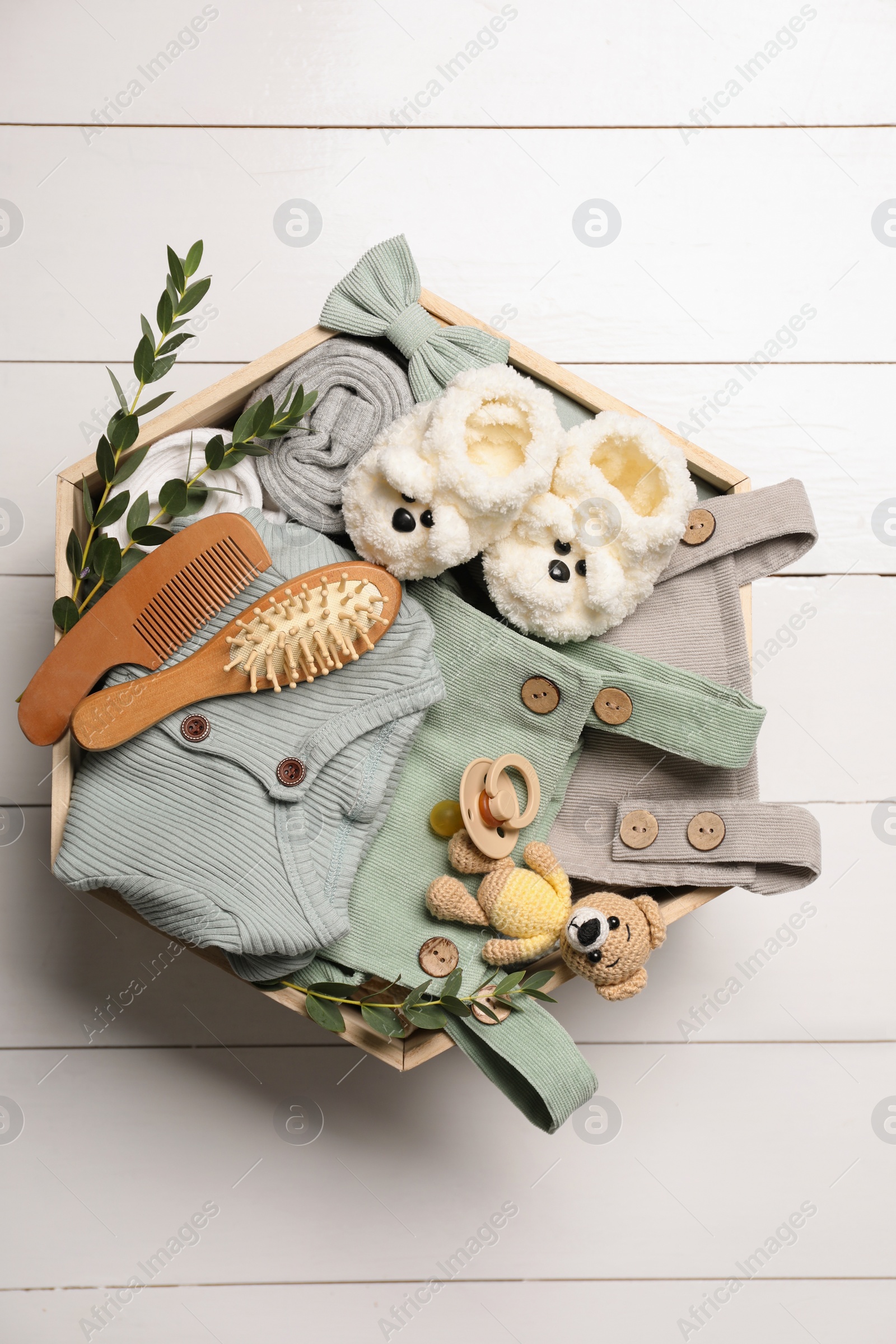 Photo of Children's clothes, shoes, toy bear and pacifier in crate on white wooden table, top view