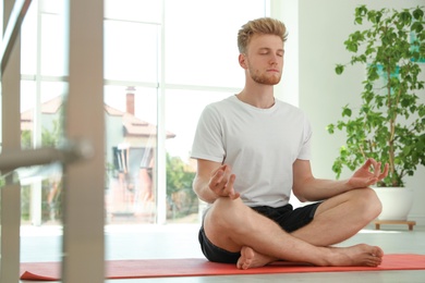 Photo of Handsome young man practicing zen yoga indoors