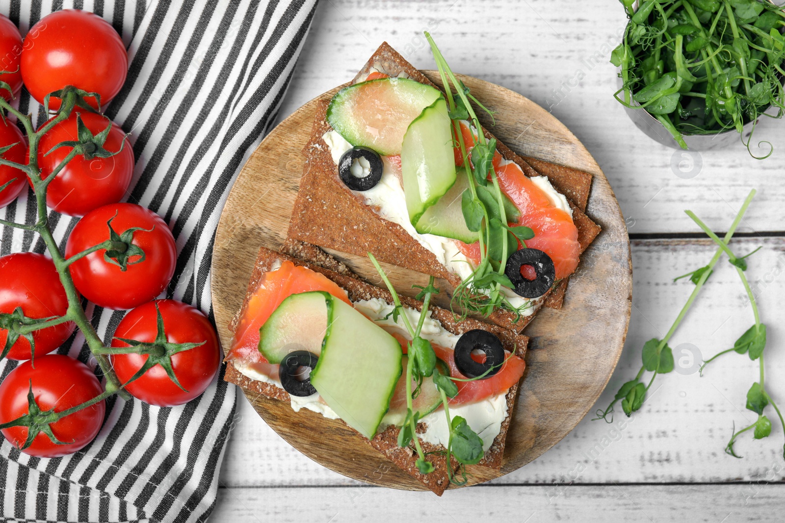 Photo of Tasty rye crispbreads with salmon, cream cheese and vegetables on white wooden table, flat lay