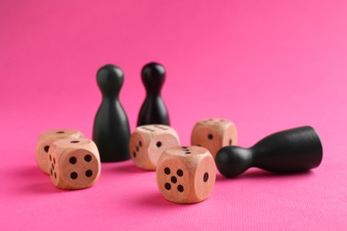 Wooden dices and color game pieces on pink background, closeup