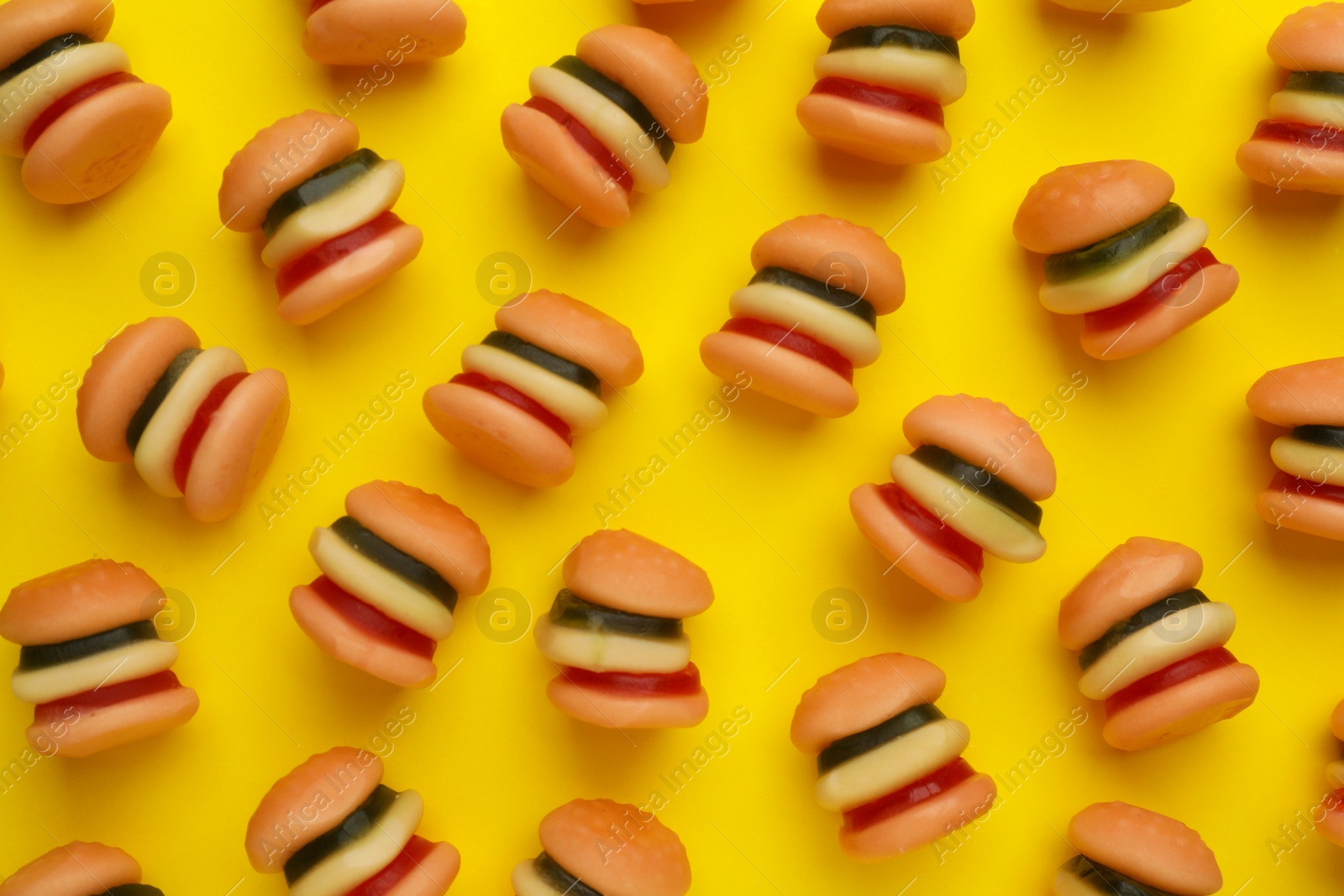 Photo of Tasty jelly candies in shape of burger on yellow background, flat lay