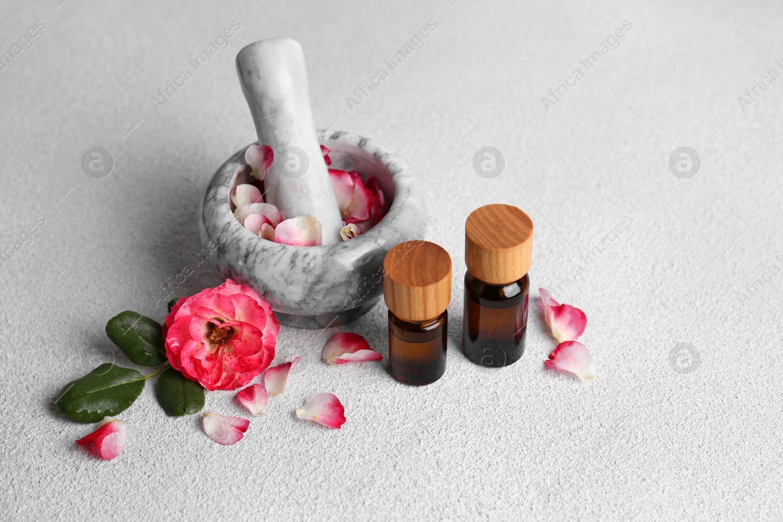 Photo of Glass bottles of aromatic essential oil, mortar with roses on white table