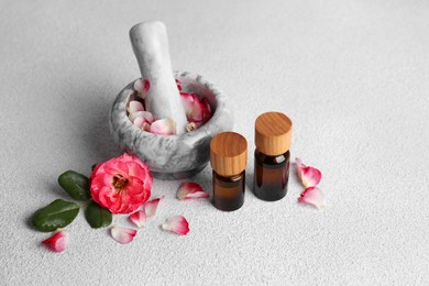 Photo of Glass bottles of aromatic essential oil, mortar with roses on white table