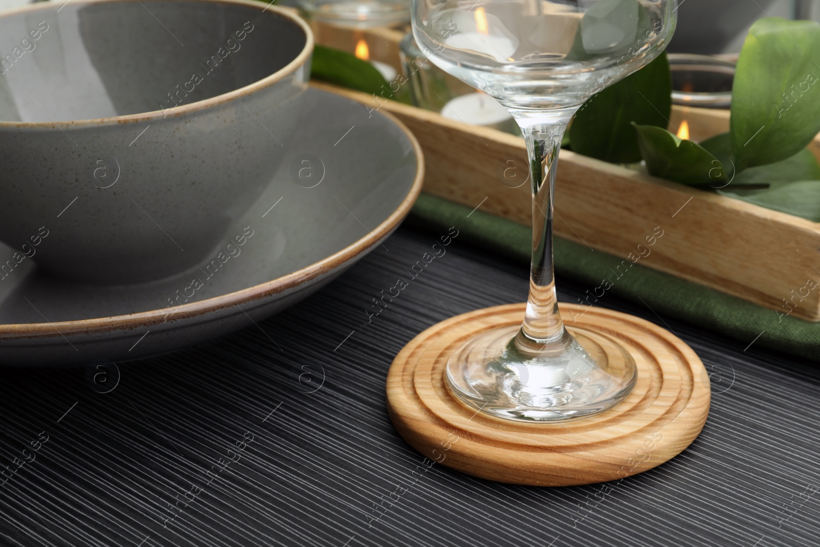 Photo of Place setting with glass and drink coaster on black wooden table, closeup view