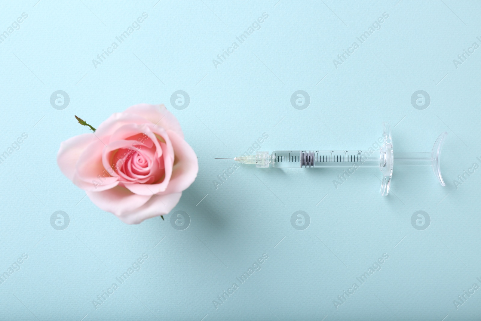 Photo of Cosmetology. Medical syringe and rose flower on light blue background, flat lay