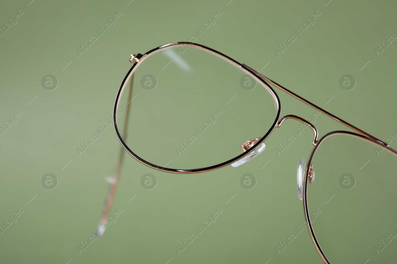 Photo of Stylish pair of glasses with metal frame on olive background, closeup